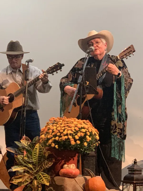 Judy James performing a duet on stage beside autumn mums